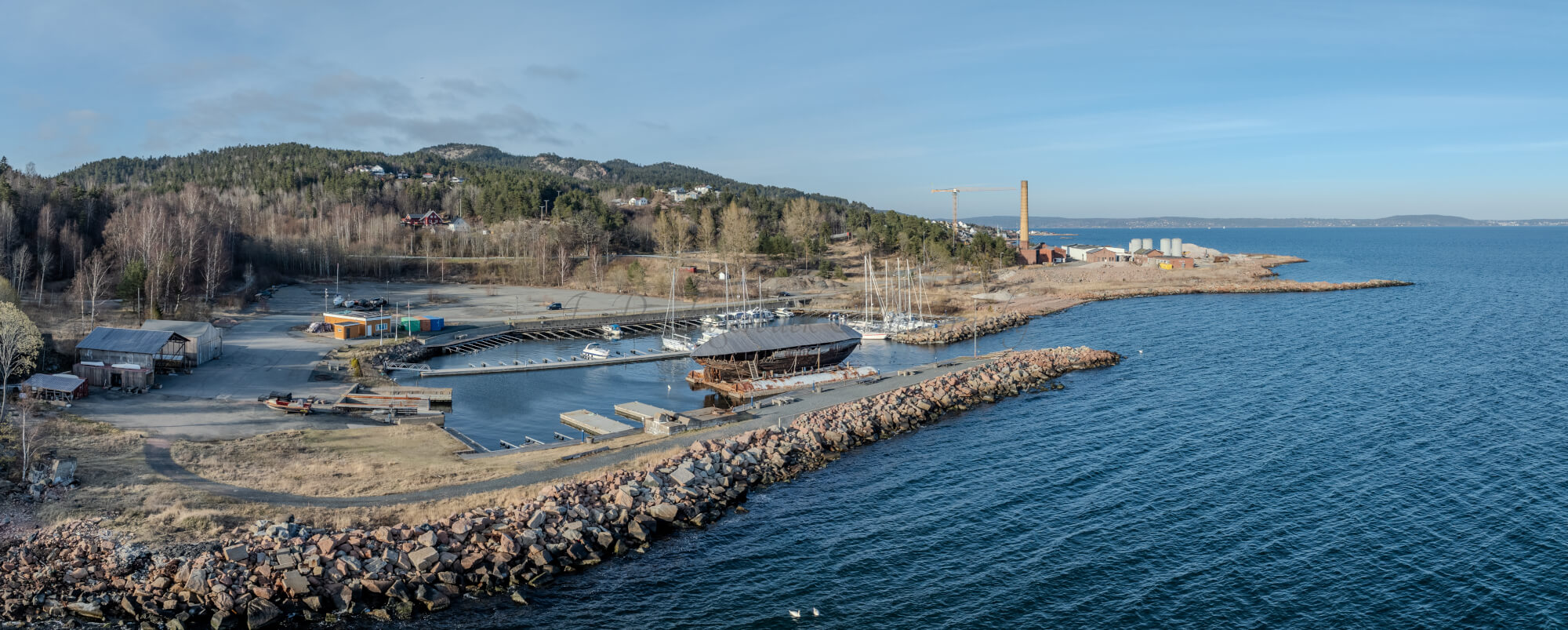 An old ship  wreck with a protection roof over it in a marina by a large body of water under a blue sky