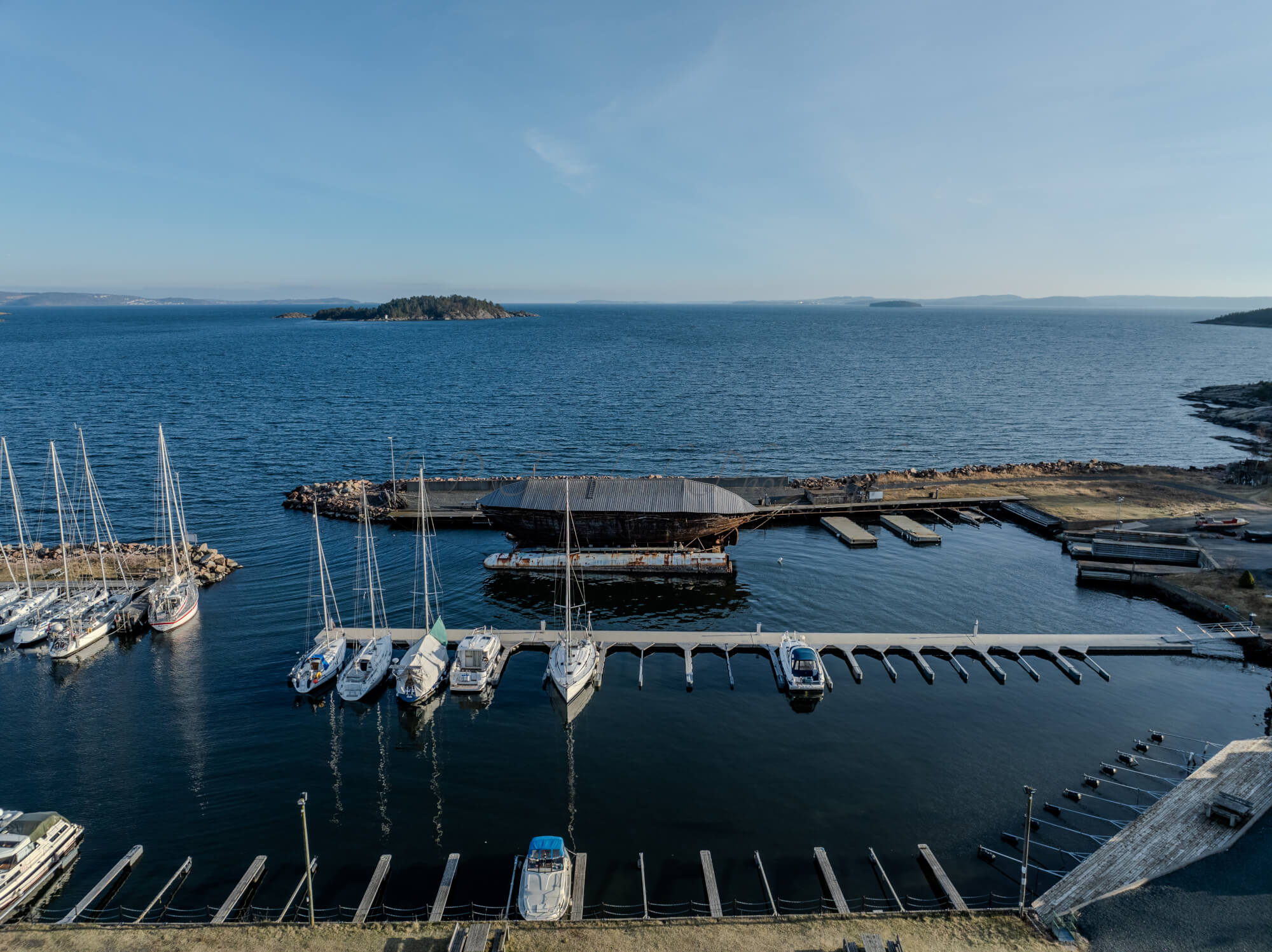 An old ship  wreck with a protection roof over it in a marina by a large body of water under a blue sky
