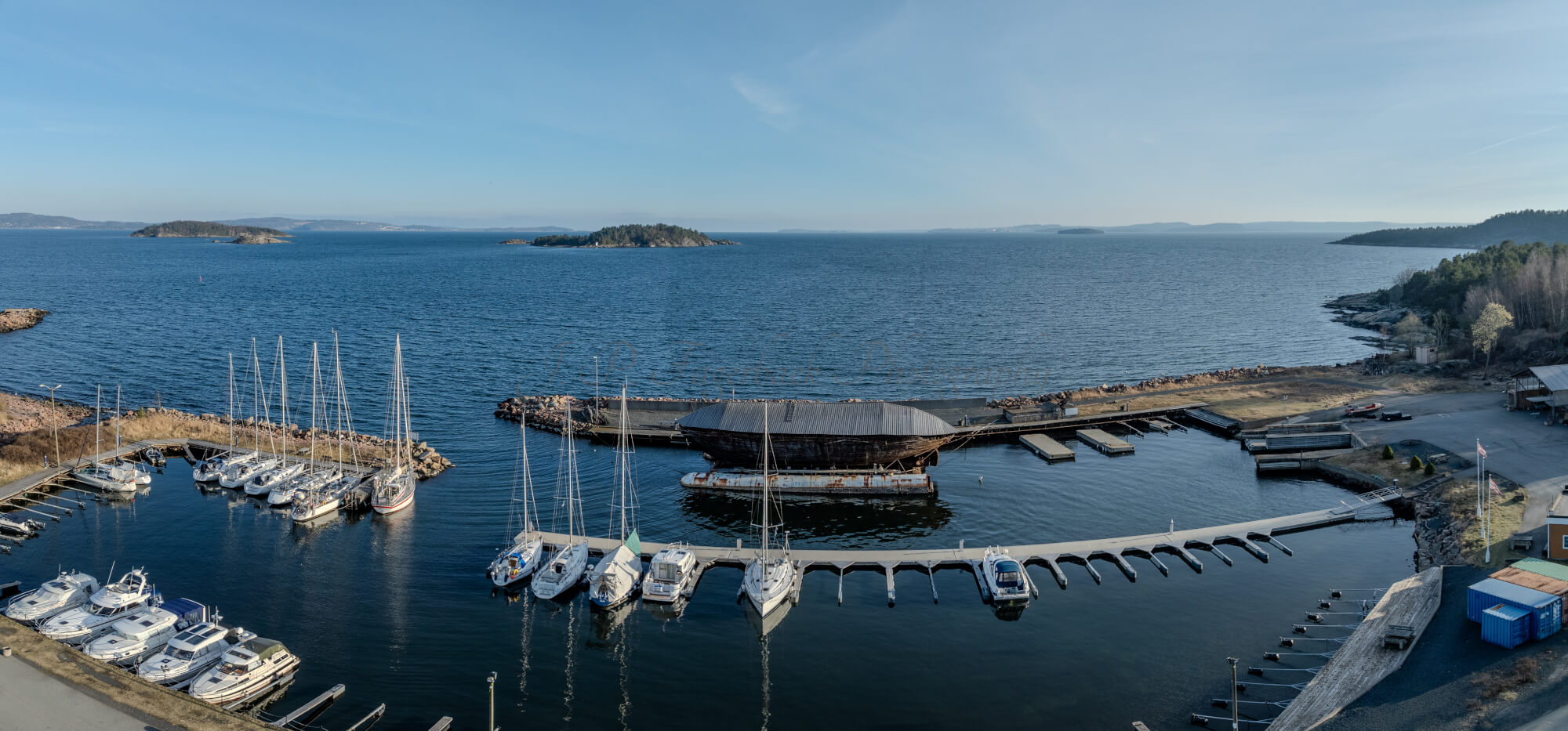 An old ship  wreck with a protection roof over it in a marina by a large body of water under a blue sky