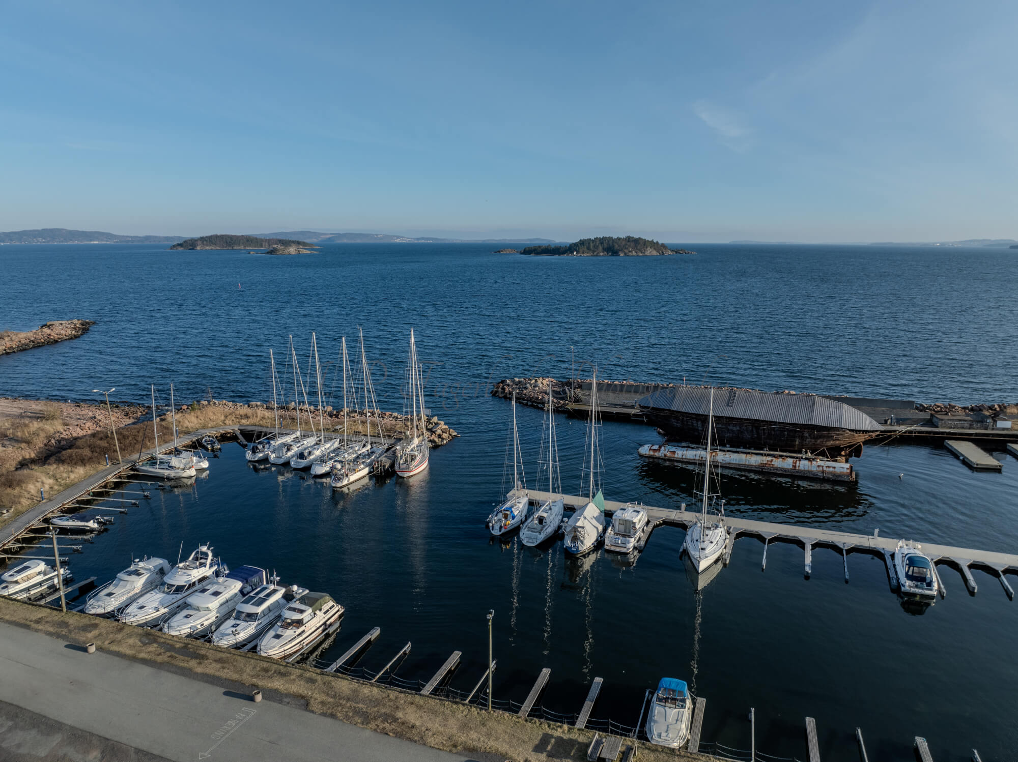 An old ship  wreck with a protection roof over it in a marina by a large body of water under a blue sky