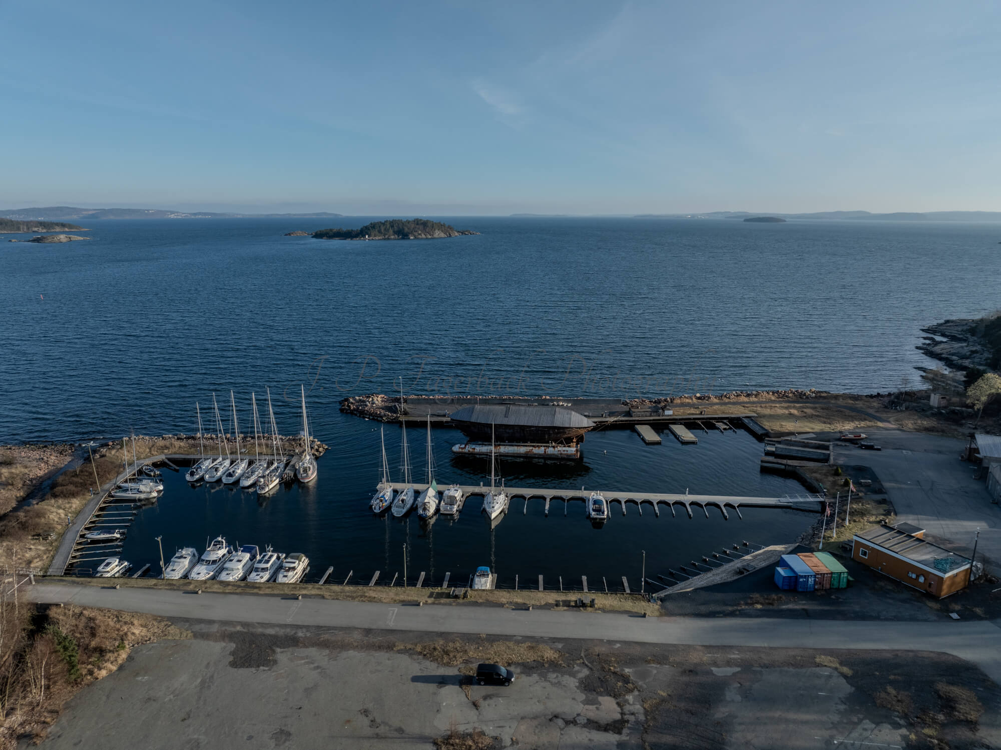 An old ship  wreck with a protection roof over it in a marina by a large body of water under a blue sky
