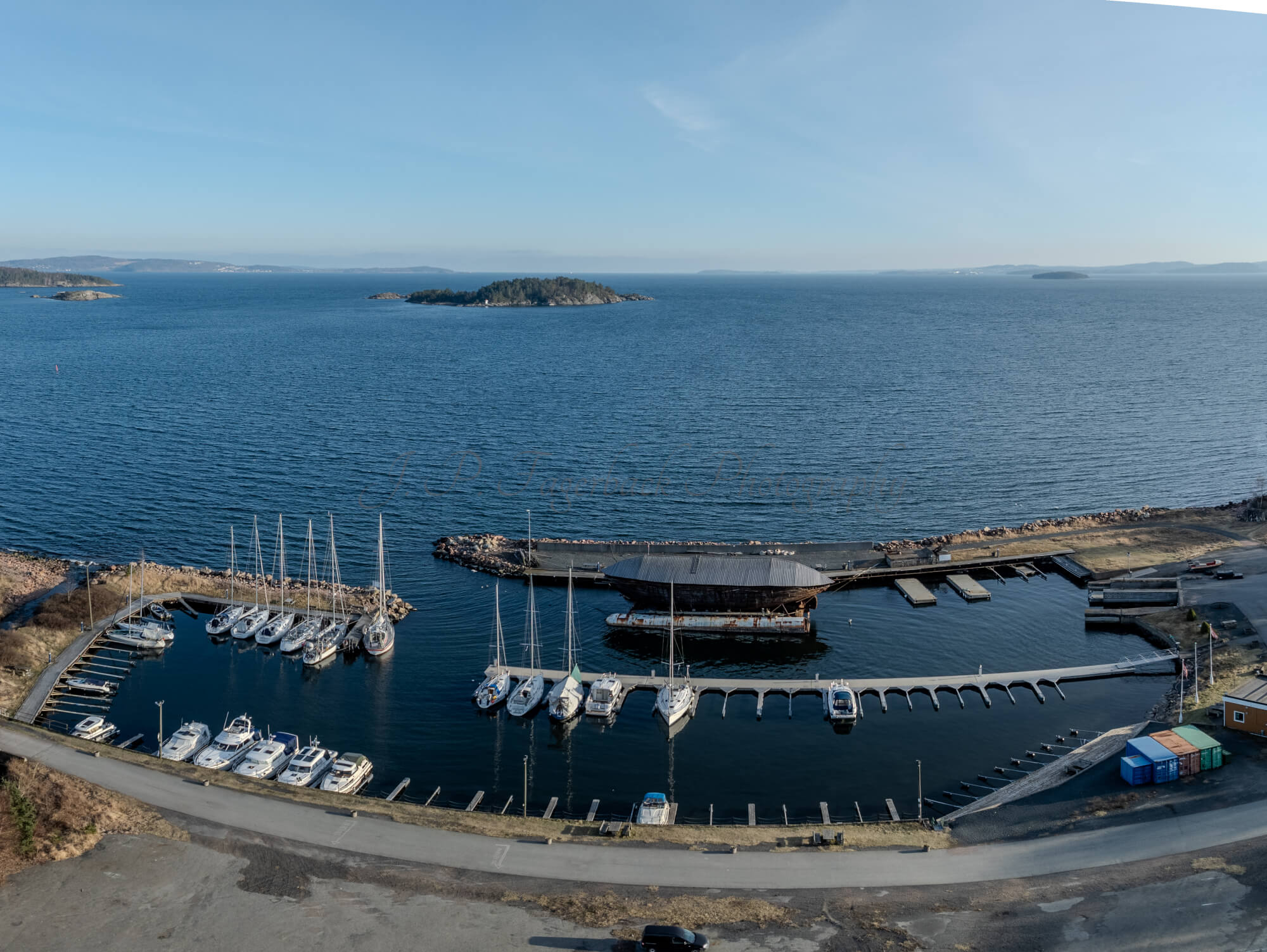 An old ship  wreck with a protection roof over it in a marina by a large body of water under a blue sky