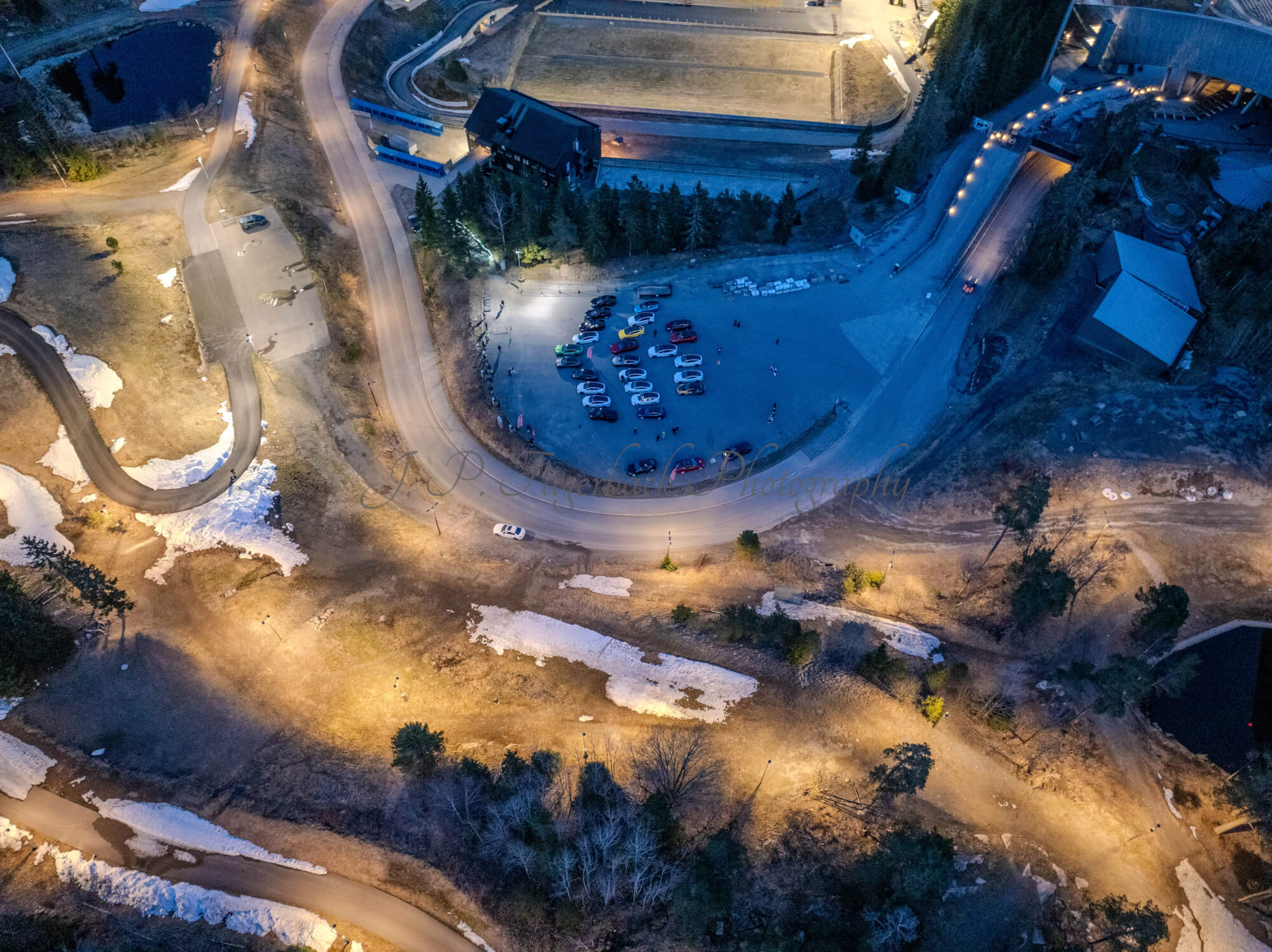 Cars on a parking lot from upon high with a ski jump in the background