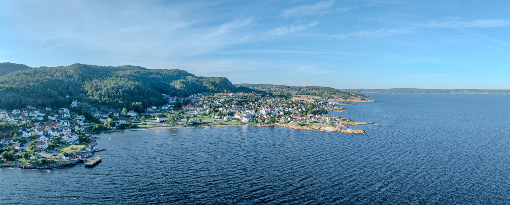 Houses of a town close to a body of water under an almost cloudless sky